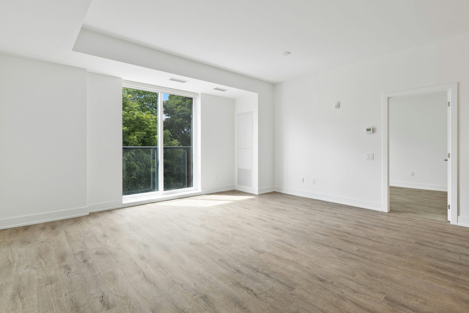 Derselbe Raum vorher: leeres Wohnzimmer mit Holzboden und bodentiefem Fenster